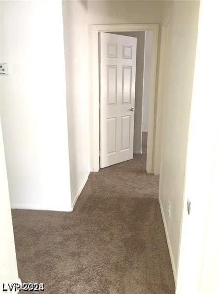 corridor featuring baseboards and dark carpet