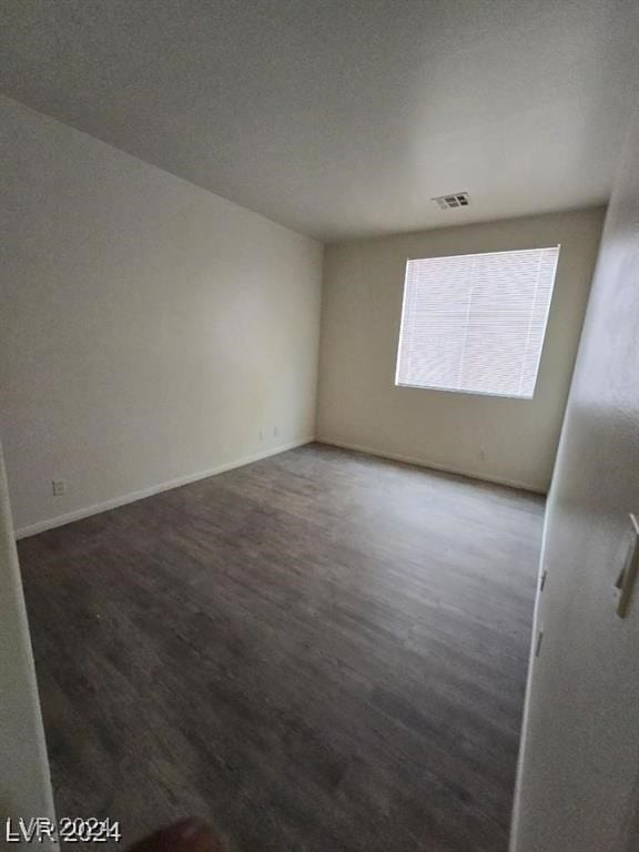 empty room with wood finished floors, visible vents, and baseboards