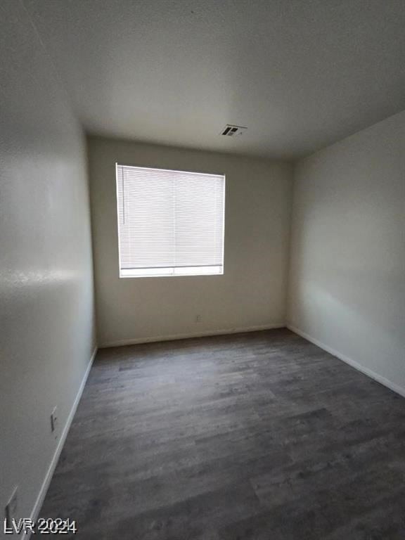 spare room with dark wood finished floors, visible vents, and baseboards