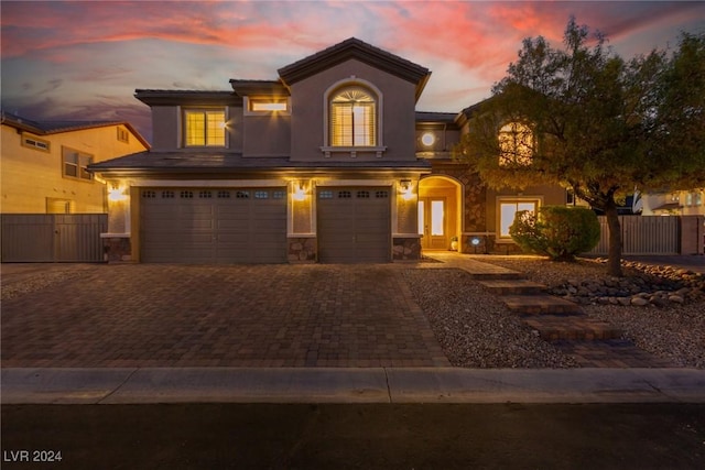 view of front facade featuring stone siding, decorative driveway, an attached garage, and fence