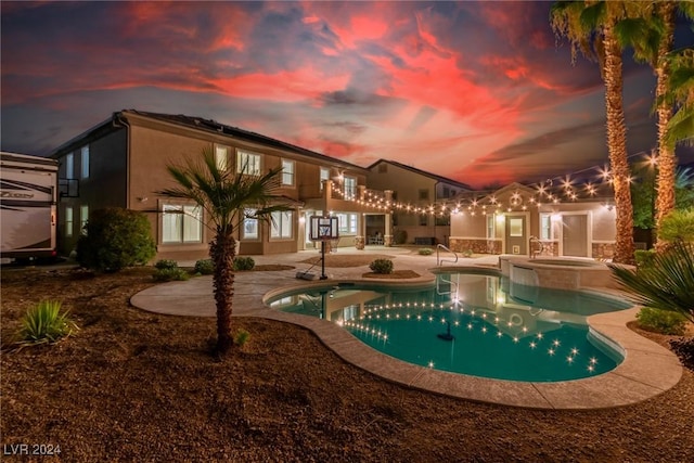 pool at dusk with a pool with connected hot tub and a patio