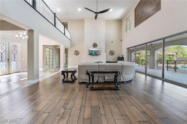 living room with ceiling fan with notable chandelier, a high ceiling, french doors, and hardwood / wood-style flooring