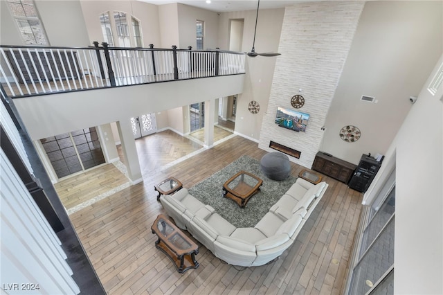 living room featuring a high ceiling, wood-type flooring, a fireplace, and ceiling fan