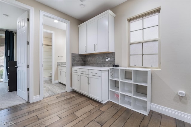 kitchen with white cabinets, plenty of natural light, light wood-type flooring, and tasteful backsplash