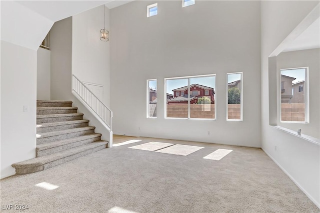 unfurnished living room with stairs, a high ceiling, and light colored carpet