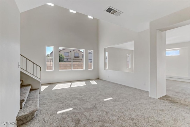 unfurnished living room featuring light colored carpet, visible vents, stairway, a high ceiling, and baseboards