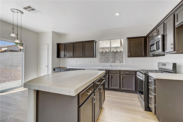 kitchen with dark brown cabinetry, stainless steel appliances, visible vents, tile counters, and a center island