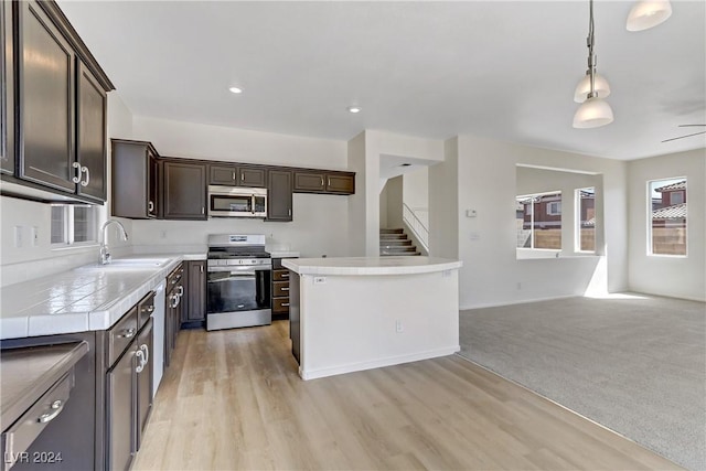 kitchen featuring decorative light fixtures, light countertops, appliances with stainless steel finishes, a sink, and dark brown cabinets