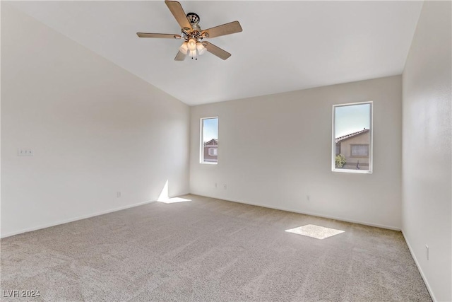 empty room featuring vaulted ceiling, light colored carpet, ceiling fan, and baseboards