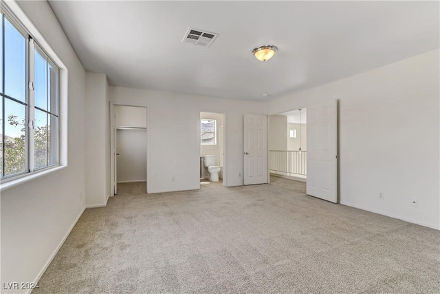 unfurnished bedroom featuring a walk in closet, visible vents, light carpet, and ensuite bath