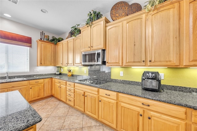 kitchen with light brown cabinets, light tile patterned flooring, appliances with stainless steel finishes, dark stone counters, and sink