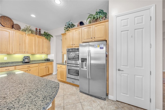 kitchen with appliances with stainless steel finishes, stone counters, light tile patterned floors, and light brown cabinetry