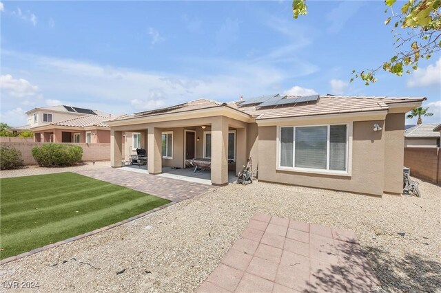 rear view of property featuring solar panels, a patio area, and a lawn