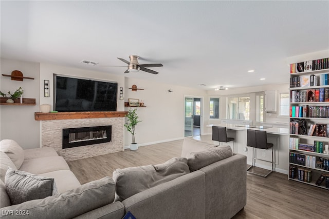 living room with ceiling fan, a stone fireplace, and hardwood / wood-style flooring