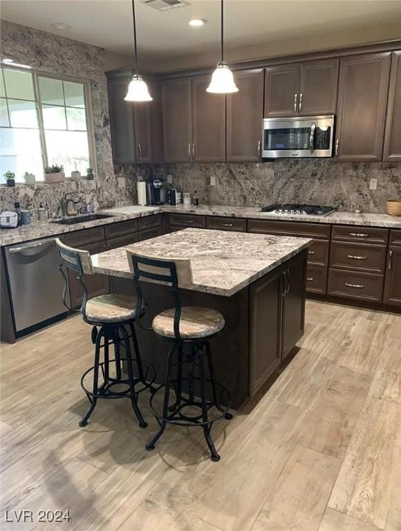 kitchen with stainless steel appliances, dark brown cabinetry, light stone countertops, a kitchen island, and decorative light fixtures