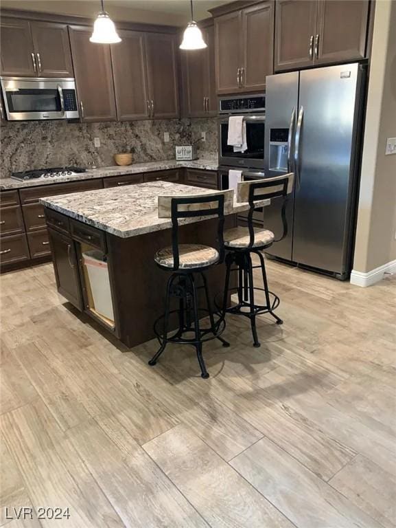 kitchen featuring appliances with stainless steel finishes, decorative light fixtures, a center island, light stone countertops, and dark brown cabinets