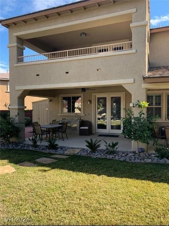 rear view of property featuring a balcony, a lawn, a patio area, and french doors