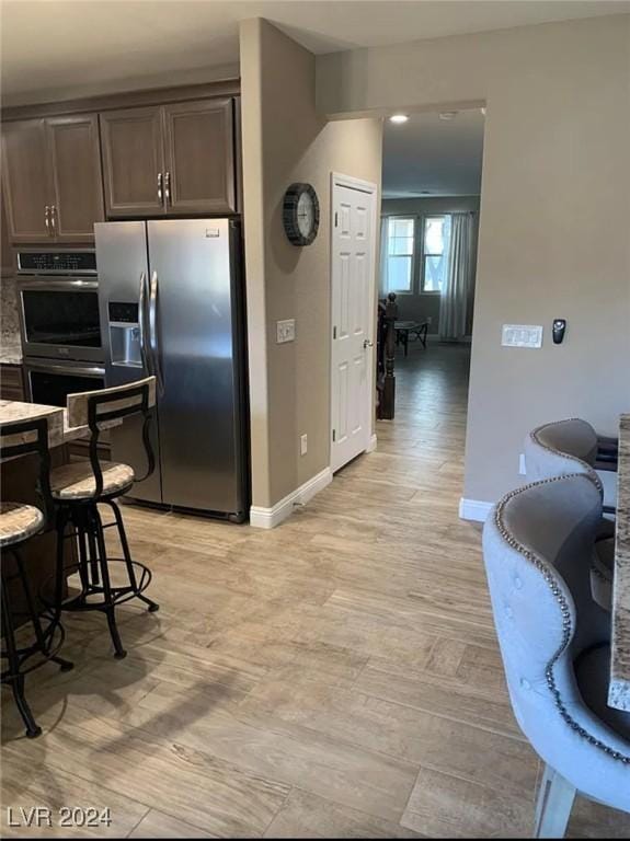 kitchen with light hardwood / wood-style floors, light stone counters, dark brown cabinetry, and stainless steel fridge with ice dispenser