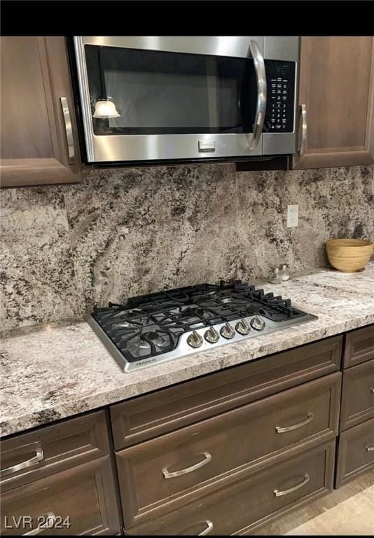 kitchen with light stone countertops, decorative backsplash, dark brown cabinets, and stainless steel appliances