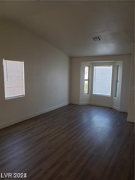 unfurnished room with dark wood-style floors, visible vents, lofted ceiling, and baseboards