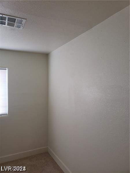 spare room with light carpet, visible vents, a textured ceiling, and baseboards