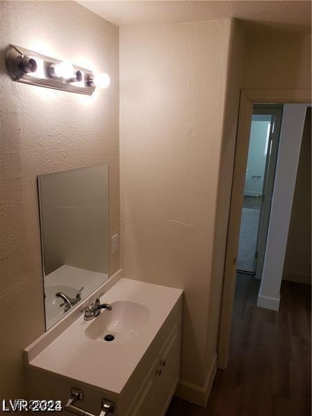 bathroom with baseboards, vanity, a textured wall, and wood finished floors