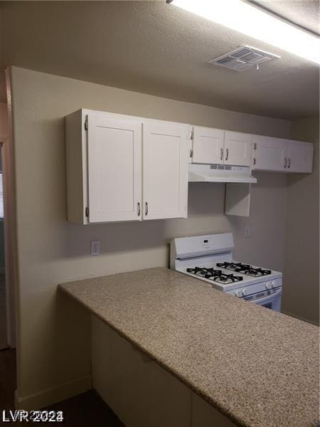 kitchen with visible vents, white range with gas stovetop, under cabinet range hood, a textured ceiling, and white cabinetry