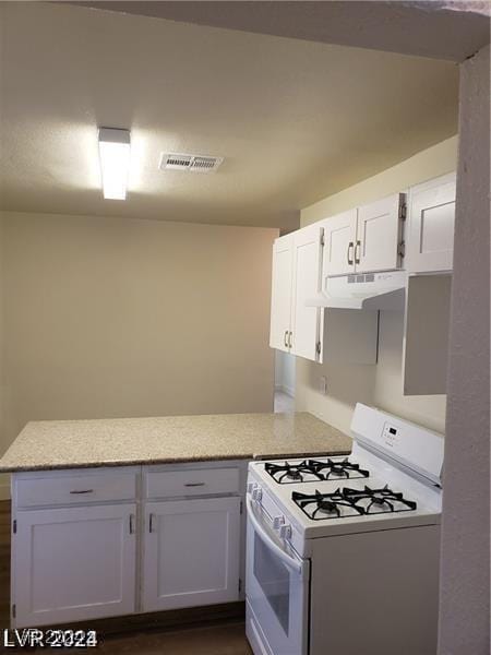 kitchen with visible vents, under cabinet range hood, light countertops, white range with gas cooktop, and a peninsula