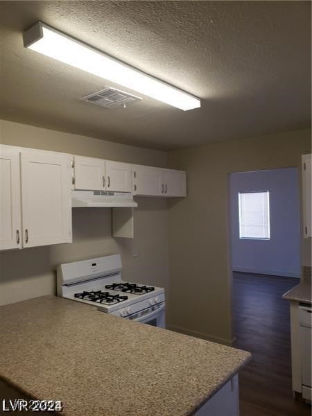 kitchen with white cabinets, dark hardwood / wood-style floors, a textured ceiling, and gas range gas stove