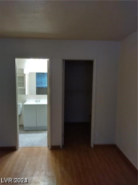 unfurnished bedroom featuring a spacious closet, connected bathroom, wood-type flooring, and a closet