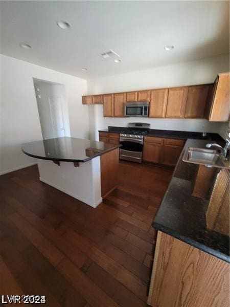 kitchen with dark countertops, dark wood-style flooring, stainless steel appliances, and a sink