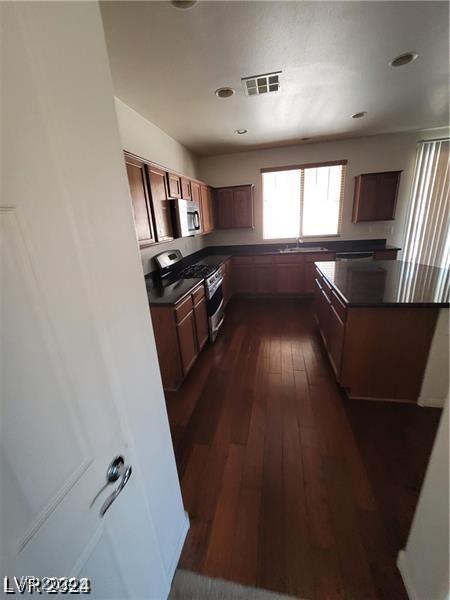 kitchen with stainless steel appliances, dark countertops, visible vents, and dark wood-style flooring