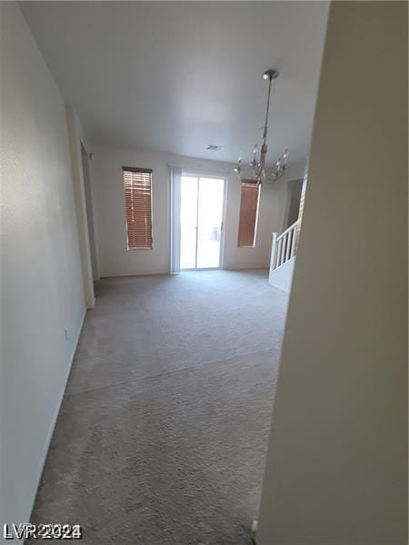 spare room featuring light colored carpet, a notable chandelier, and stairway