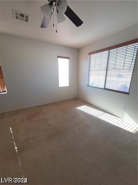 empty room with visible vents, a ceiling fan, and carpet floors