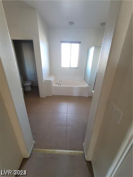 full bath featuring toilet, a bath, and tile patterned flooring