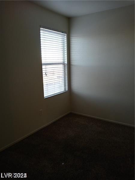 empty room featuring baseboards and dark colored carpet