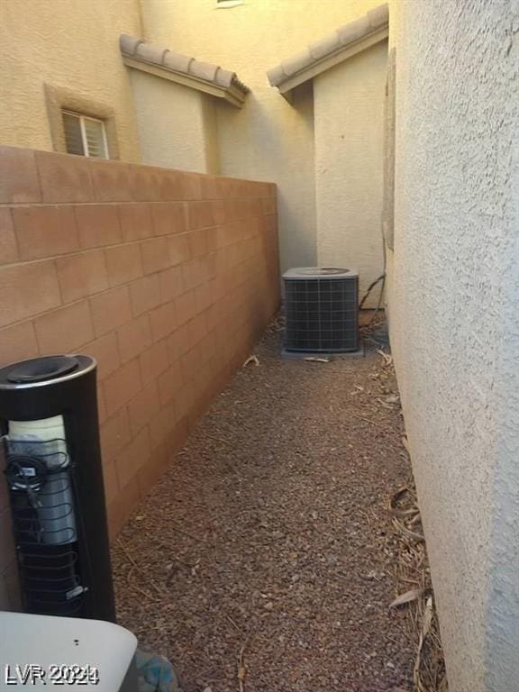 view of side of home with a tile roof, stucco siding, central AC, and fence