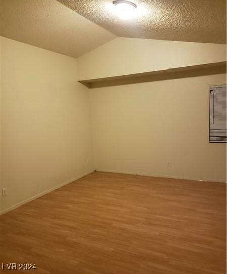 empty room with a textured ceiling, hardwood / wood-style flooring, and vaulted ceiling