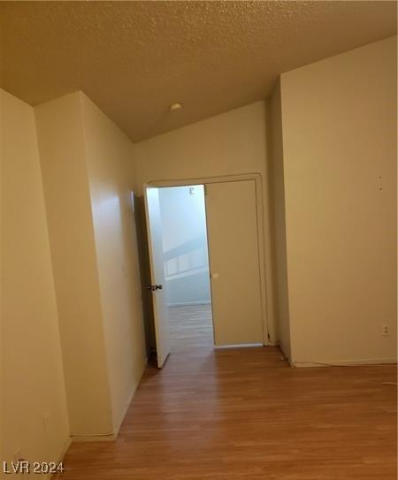 corridor featuring a textured ceiling, wood-type flooring, and vaulted ceiling