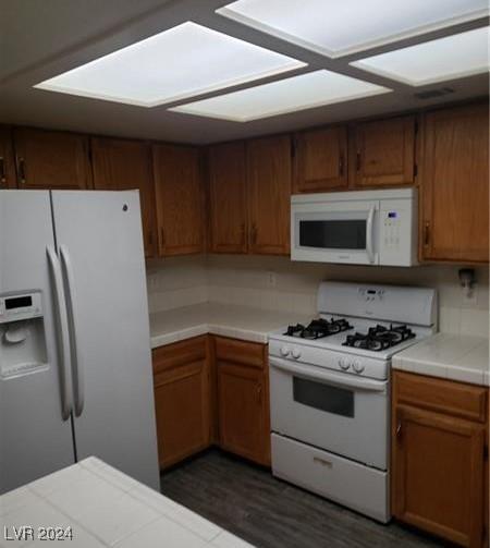 kitchen with dark hardwood / wood-style flooring, tile counters, and white appliances