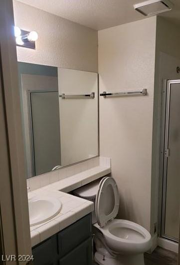 bathroom with walk in shower, toilet, vanity, and a textured ceiling