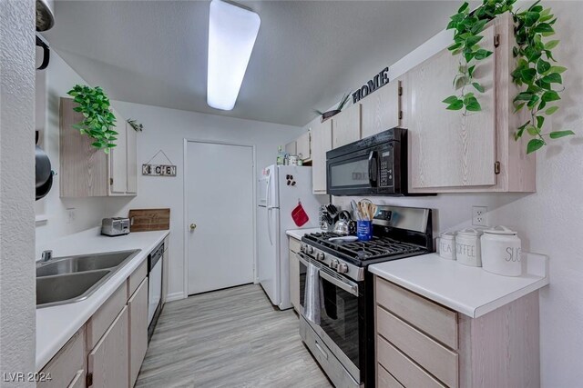 kitchen with stainless steel appliances, sink, light brown cabinetry, and light hardwood / wood-style floors