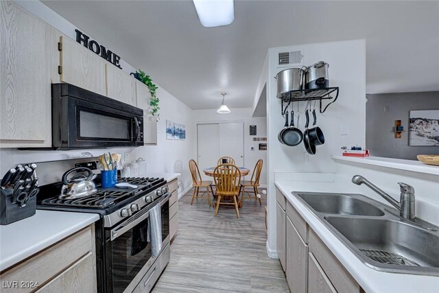 kitchen featuring light brown cabinetry, sink, stainless steel gas range, and light hardwood / wood-style flooring