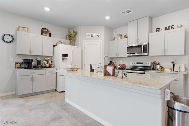 kitchen featuring stainless steel appliances, white cabinets, light stone counters, light tile patterned floors, and a kitchen island with sink