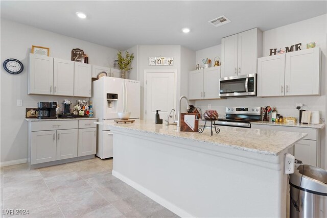 kitchen featuring white cabinetry, appliances with stainless steel finishes, light stone countertops, and an island with sink