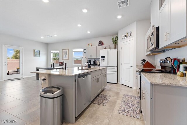 kitchen featuring stainless steel appliances, light stone countertops, sink, and a center island with sink