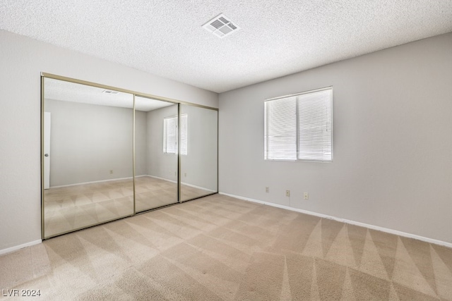 unfurnished bedroom featuring light carpet, a closet, and a textured ceiling