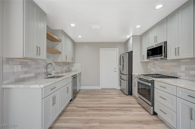 kitchen featuring stainless steel appliances, a sink, light stone countertops, open shelves, and light wood finished floors