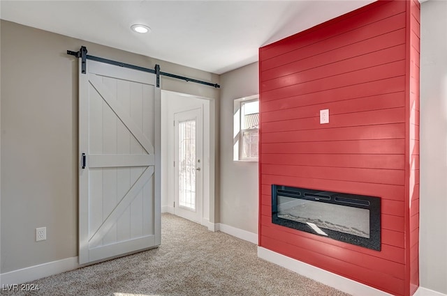 interior space with carpet, a barn door, baseboards, and a glass covered fireplace