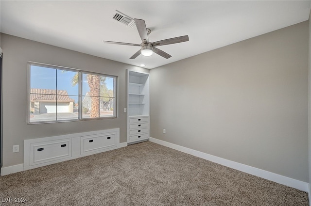 carpeted empty room with built in features, visible vents, baseboards, and a ceiling fan